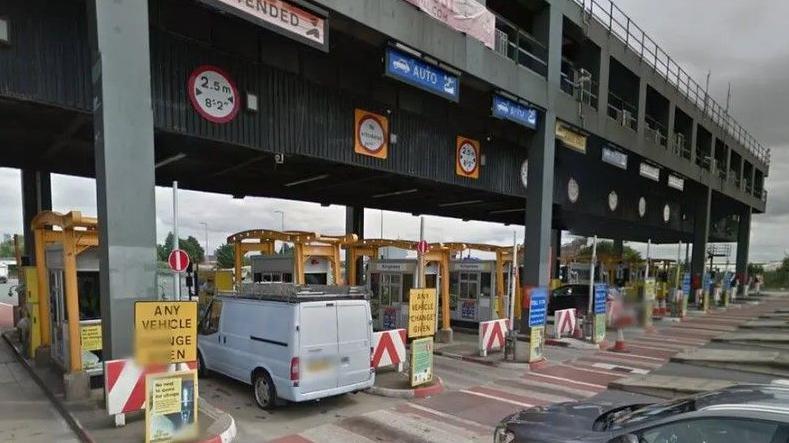 Cars and vans queue up ready to go through the Mersey tunnel toll booths, with signs including 'any vehicle change given'.