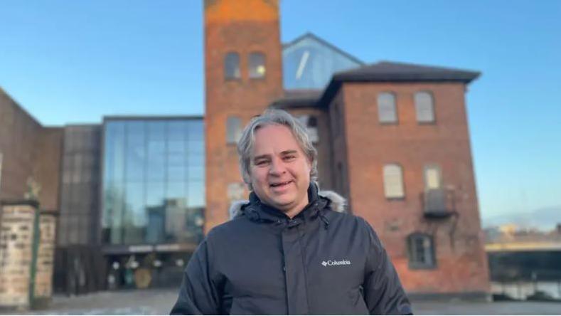 Tony Butler in front of the Musuem of Making in Derby - he is wearing a black coat