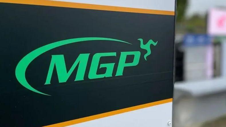 A sign reads MGP in green on a black background; the three legs of man form part of the logo on the top right of the sign.