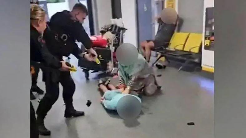 Two police officers point a laser at a man on the floor of an airport