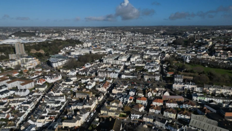 Ariel shot of South St Helier, Jersey. There are rows of houses and buildings below. The photo was taken on a cloudy day.

