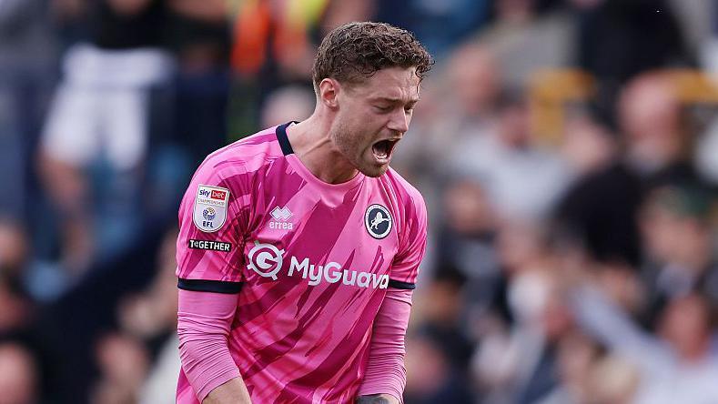 Millwall's Lukas Jensen, wearing a pink goalkeeper shirt, celebrates