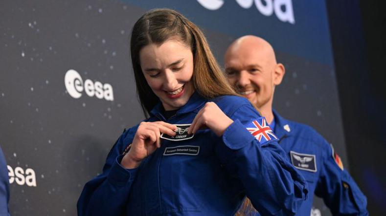 Rosemary Coogan wearing a blue jumpsuit putting on a black badge. 