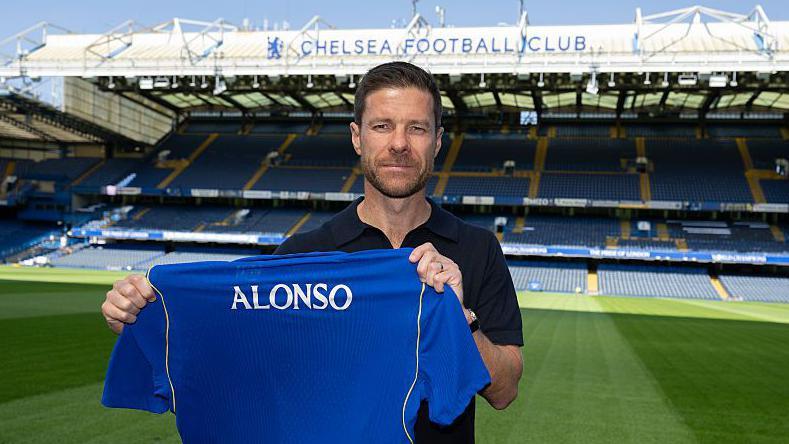 Xabi Alonso at Stamford Bridge holding a shirt with his name on the back