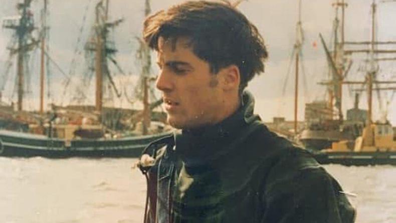An old photo of Gabe's uncle Alex, wearing deep sea diving gear. He has short dark hair and has his eyes closed facing off to the left. Ships with masts can be seen in the background.