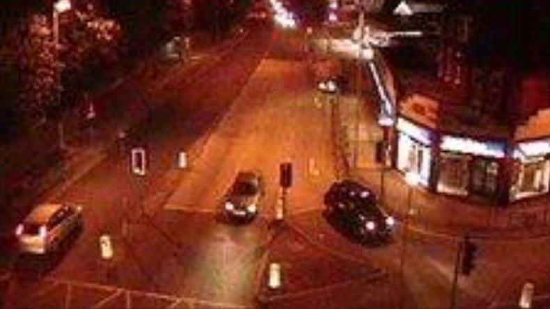 A still from CCTV footage showing a Ford C-Max car at a traffic light heading away from the camera, with a silver car and a black Hackney cab coming in the opposite direction.