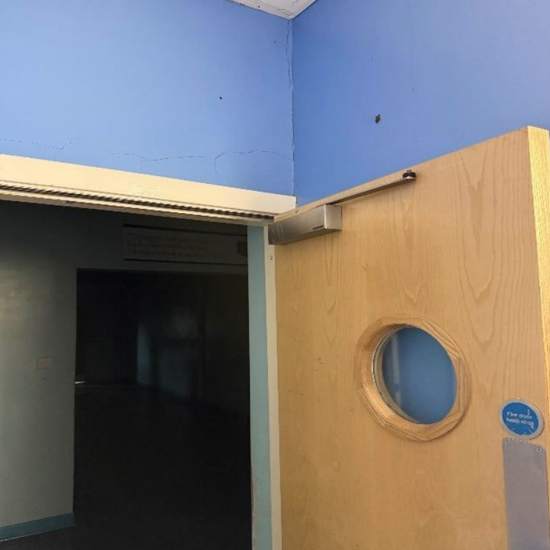 A fire door in a school, sitting wide open, with a broken self-closer.