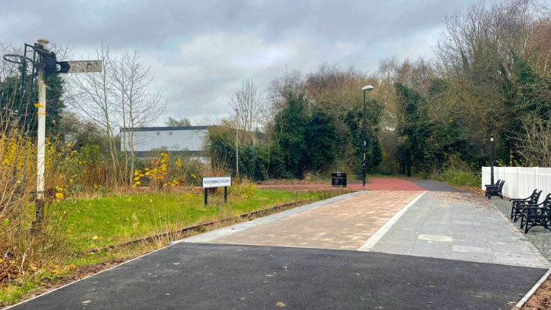 A railway platform next to a disused overgrown track.  A signal post can be seen on the left of the image
