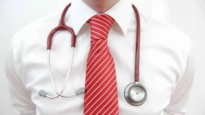 A close up of a man's chest. He is wearing a white shirt and red tie and has a red and silver stethoscope hanging around his neck.