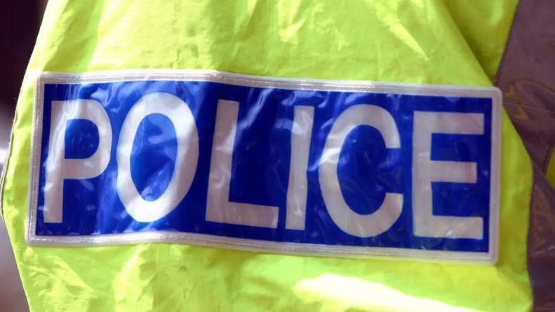 The back of a police officer wearing a yellow hi-vis with police in white capital letters written on a blue background