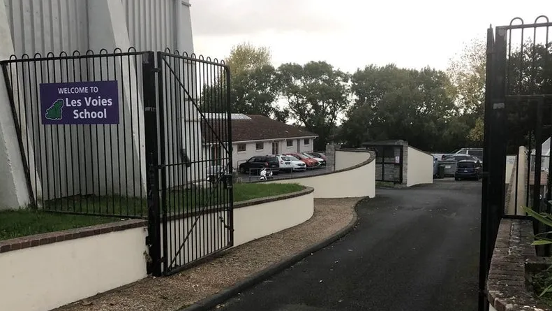 A black school gate opened, with a sign saying Les Voies School on the fence. 