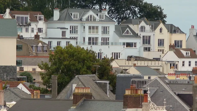 Rows of homes in one area in Guernsey, with trees and blue skies behind.