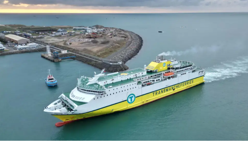 A picture of a DFDS boat in Jersey. It is bright yellow and has white throughout it. On the sea with a harbour behind.