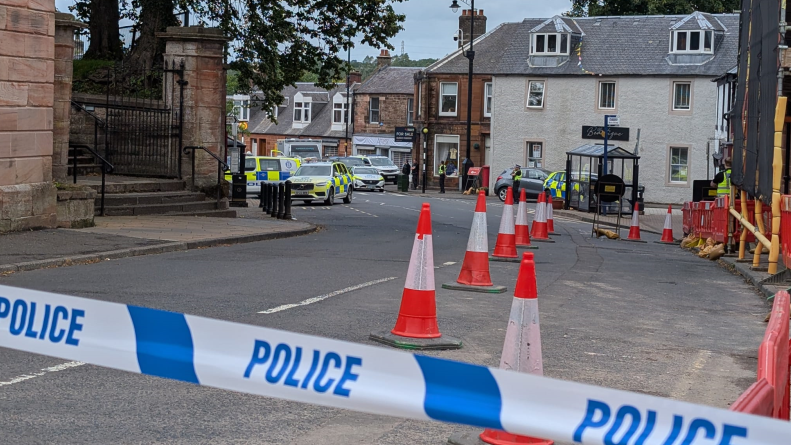 police tape seals off a road which has several police cares parked outside a row of houses