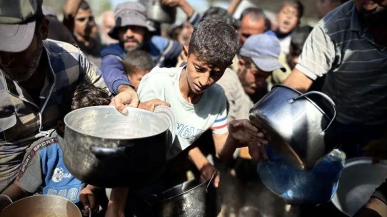 Palestinian children wait in line to receive the food distributed by charitable organizations in Khan Yunis