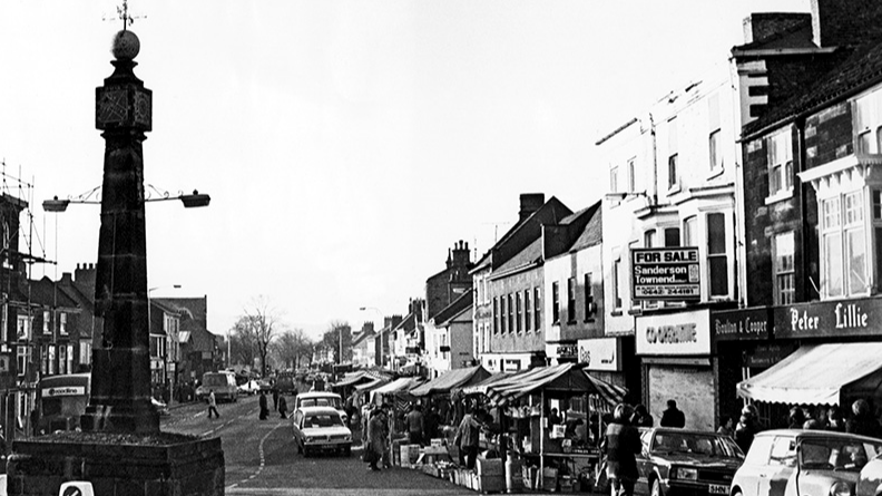 Vintage black and white photograph of Guisborough's market, with shoppers and cars