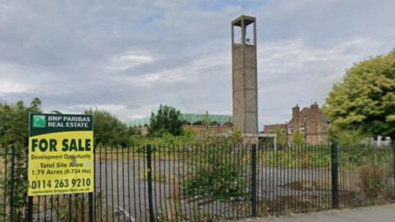 Derelict site of former pub next to 20th century church with large tower