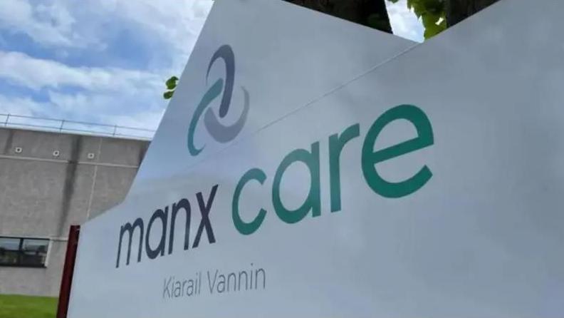 A large white sign for Manx Care, which has the name in English and Manx Gaelic in green and grey lettering.