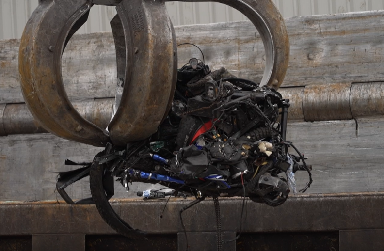 A large metal claw lifts up a clump of bikes that have been crushed