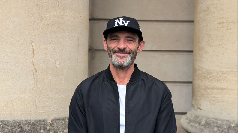 Paul Jennings wearing a baseball cap and a black jacket and looking at the camera