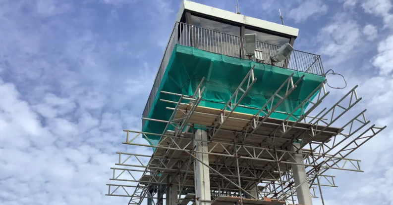 An airport control tower covered in scaffolding and a green plastic tarpaulin. 