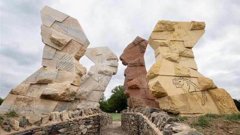 Four stone sculptures with etched drawings on the side. There are two on each side of a stone path.
