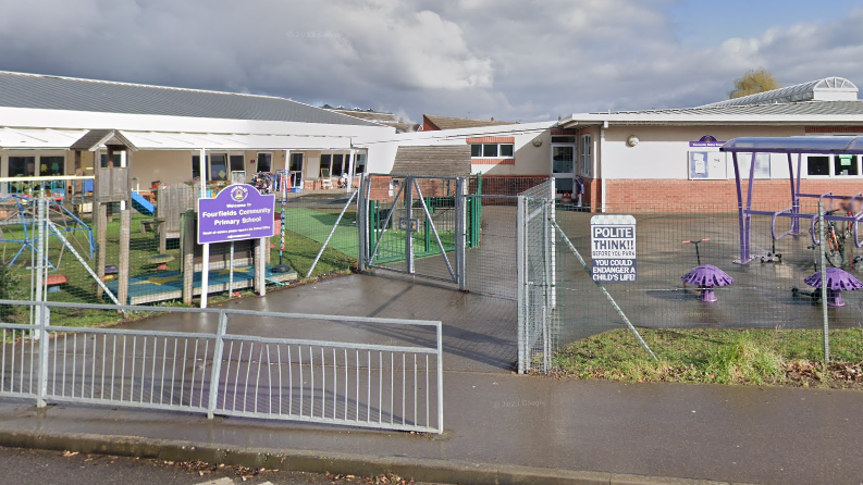 Street view of the school with metal railings in front and a purple board with the school name 