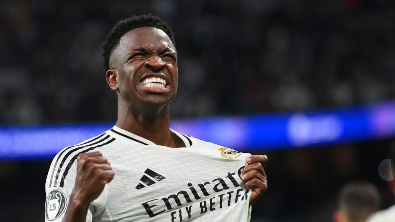 Vinicius Junior celebrates while wearing Real Madrid's white shirt and grabbing close to the club badge