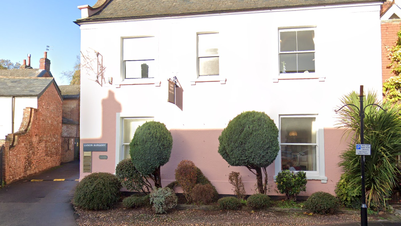 A screenshot of Google street view. It's the external of the building, which is painted pink, and the sun is making the top half of the building very bright. 