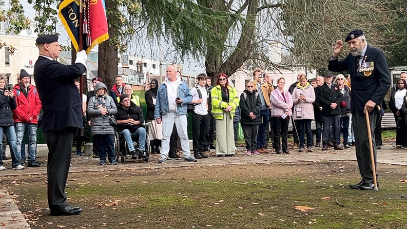 A veteran salutes a flag bearer as a line of spectators watch
