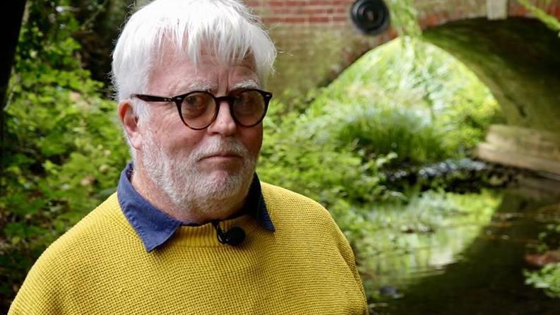 Eamonn O'Nolan standing next to the River Alde with a red brick bridge behind him