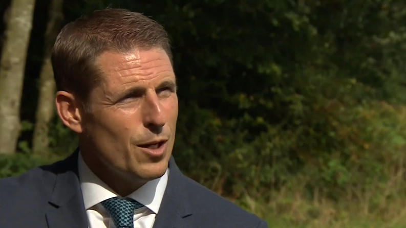 Head teacher Drew Povey, wearing a blue suit and tie, speaking to a journalist who is off camera