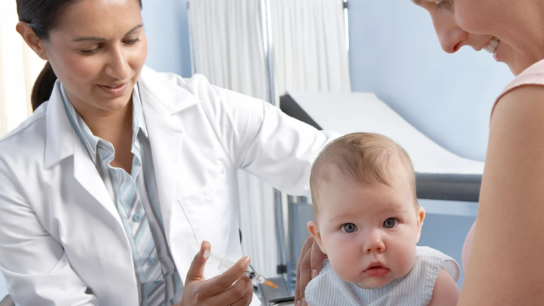 A baby is given an injection by a doctor with Mum smiling on 