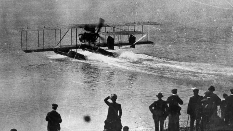 A seaplane lands on the sea in Brighton with crowds watching in the early years of the 20th Century