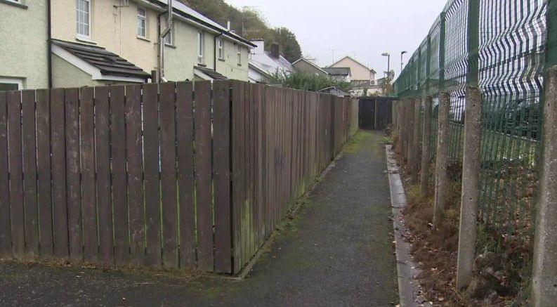 An alleyway behind a row of houses behind a wooden fence