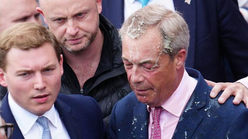 George Cottrell, left, stands alongside Nigel Farage, whose face is covered in milkshake, after a woman threw it at him in Clacton in June 2024.