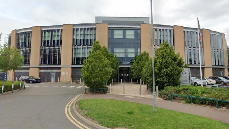 Semi-circular three-storey glass and concrete office building with trees