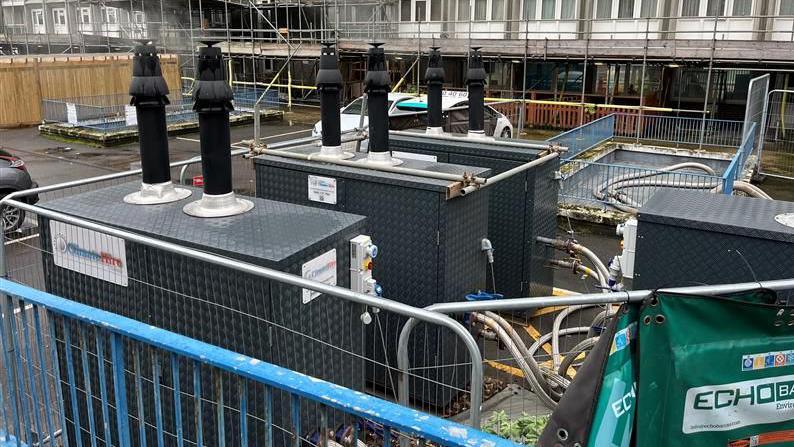 Temporary large metal boilers with chimneys on the top in the car park of the flats