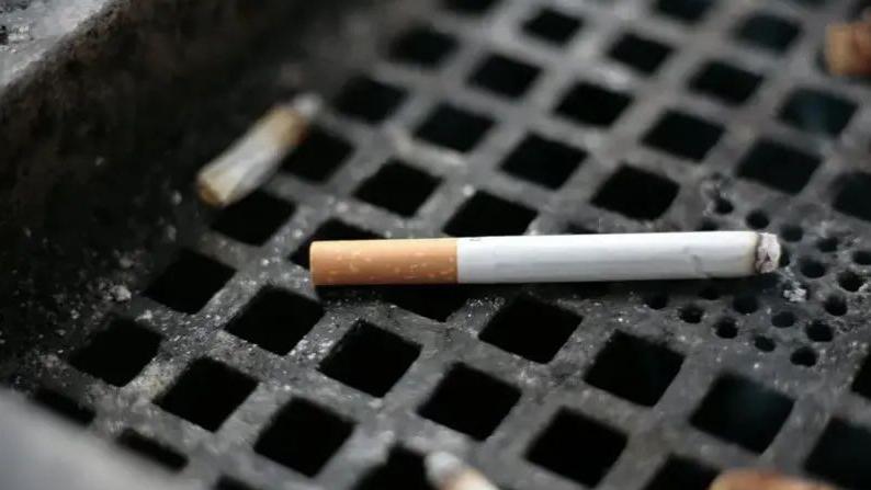 A close-up of semi-smoked cigarette on the square grill of a public ashtray.