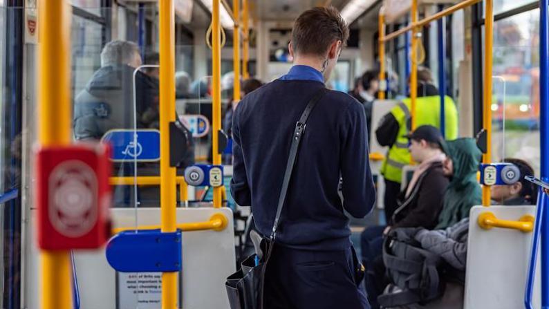 A tram conductor in a navy blue uniform with short dark hair is collecting fares from passengers