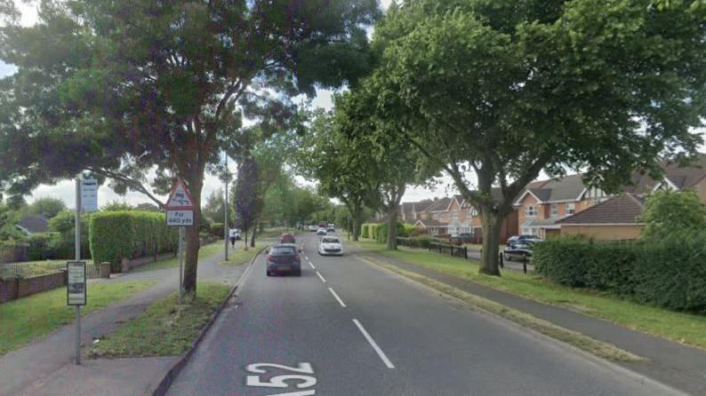 Google Streetview image of Barrowby Road, Grantham. There is a bus stop to the left and several large trees along the road. 