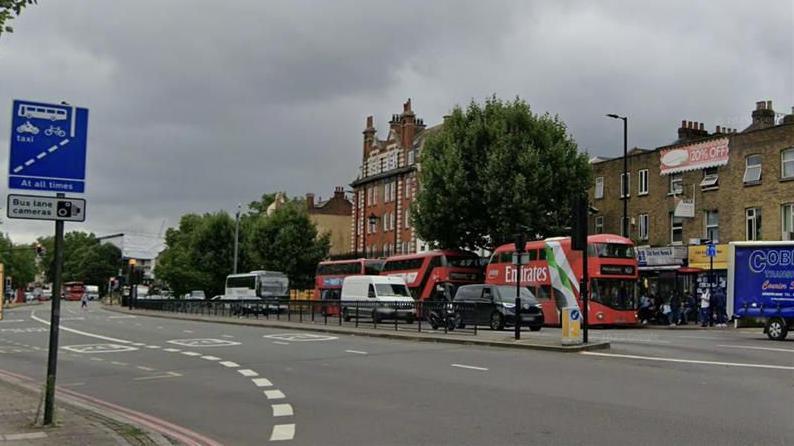 A streetview of where Dunton Road meets Old Kent Road. A bus lane, which a sign indicates is shared with cyclists, is seen alongside two other lanes on one side of the road