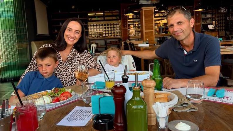 Alina Kalcheva, pictured here with her husband and children, sitting at a table in a restaurant