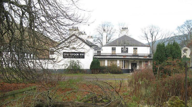The old Crook Inn site in Tweedsmuir with white walls and black signage viewed through trees