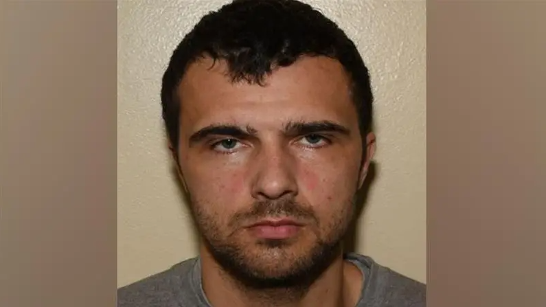 A police mugshot of Elias Morgan. He has dark hair and is wearing a grey tshirt.