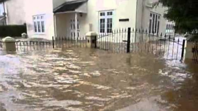 Flood water almost reaching the windows of a cream house and half-submerging the gates outside.