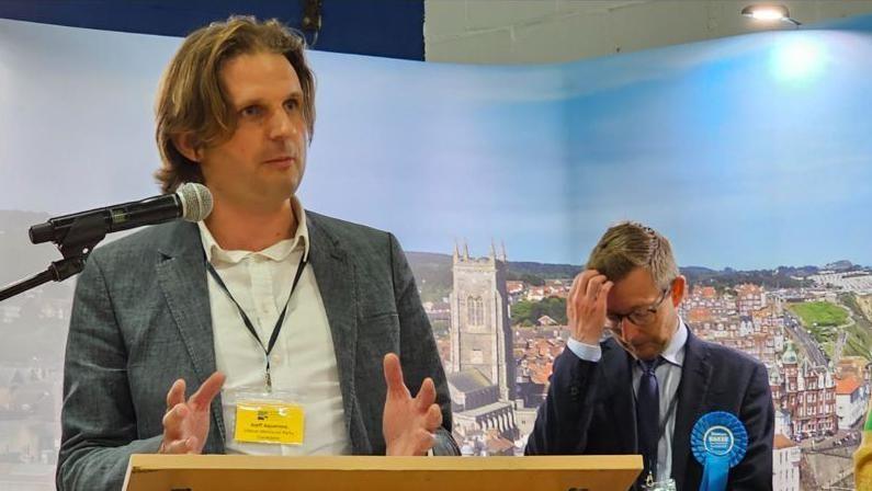 Steff Aquarone giving his winner's speech with Duncan Baker in the background