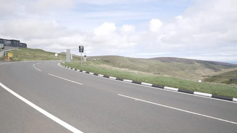 The Mountain Road at the Bungalow. The road sweeps round on the left with the Laxey Valley on the left. The Victory Cafe, which is black rectangular building, is on the hillside on the left.