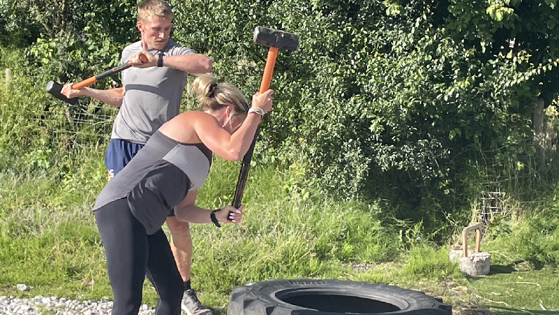 Woman and man in the sunshine hitting a large tyre with hammers