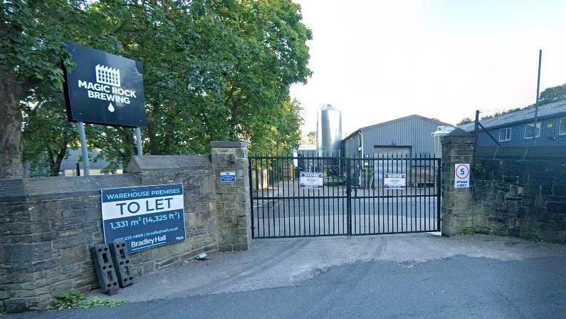 An entrance sign next to a wall and a gate which says Magic Rock Brewing.